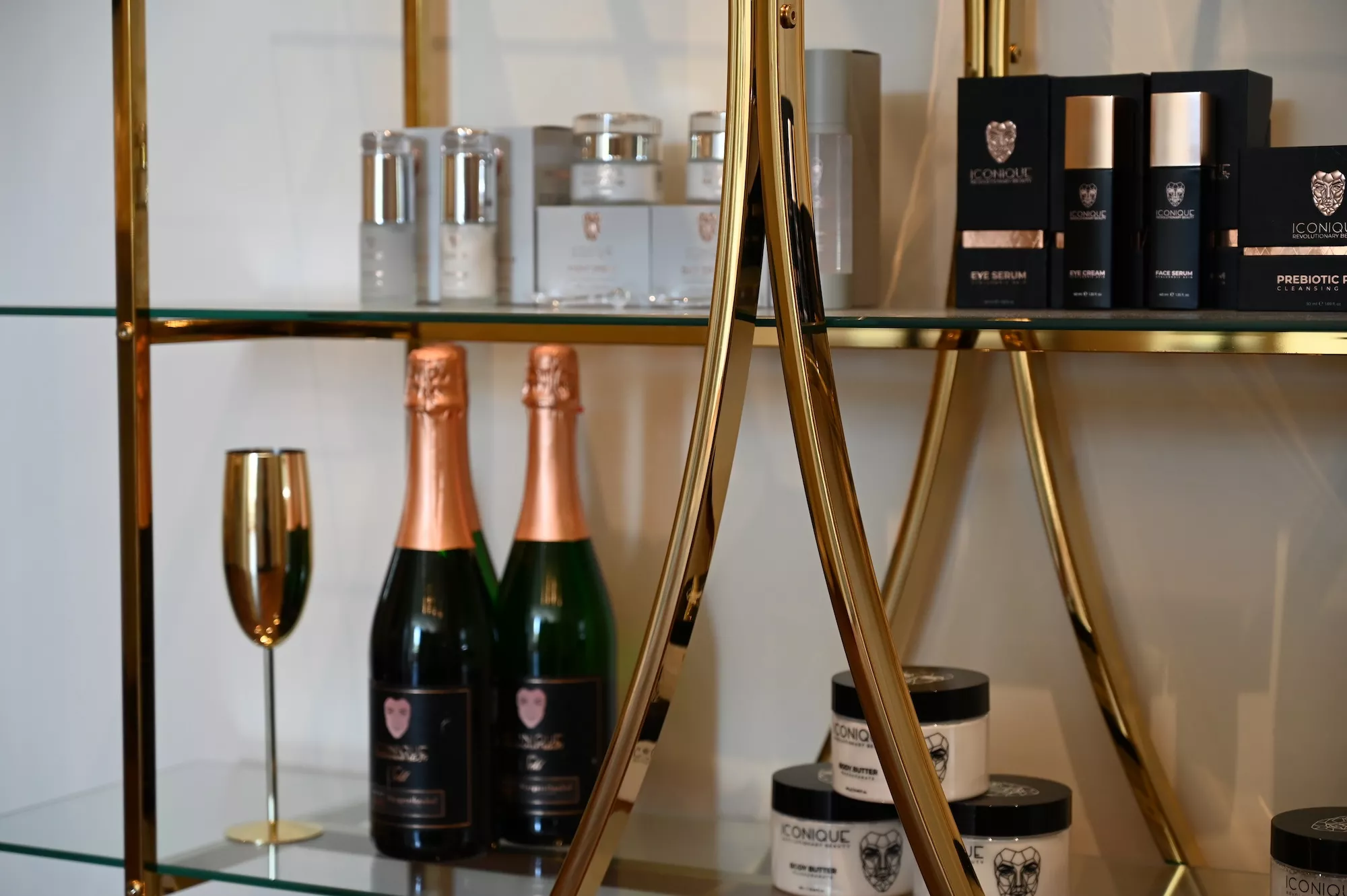 Goldenes Produktregal mit Iconique-Pflegeprodukten und Champagner