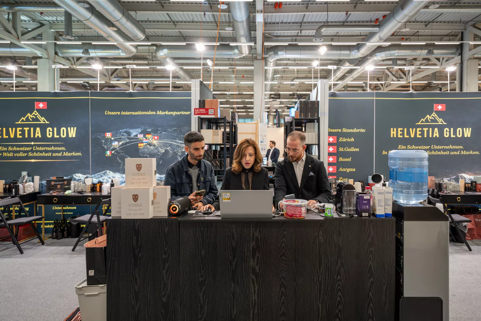 Helvetia Glow Messestand mit Team am Empfangstresen und Produktpräsentation